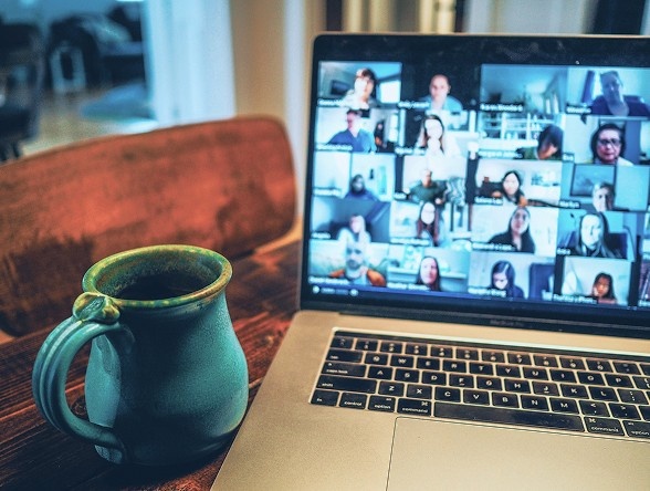 A laptop showing a zoom call with a grid of faces and a mug sit on a table.