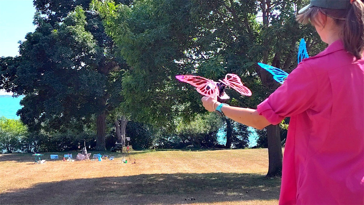 Person holding two Robot Butterflies (one red, one blue) with the event setup in the background