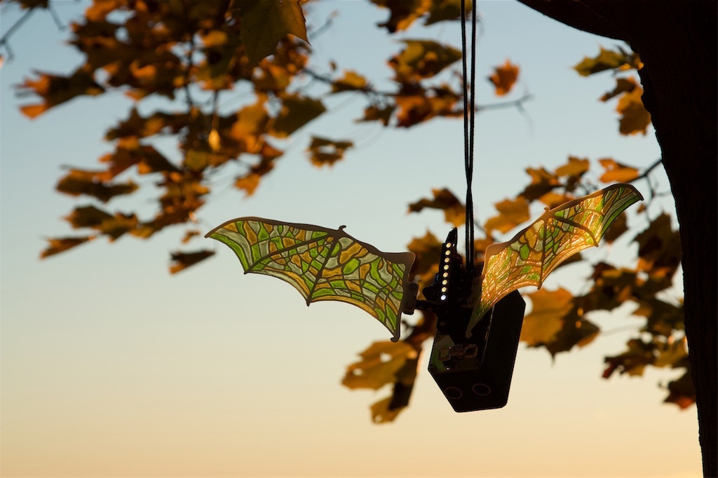 Multi coloured bat wings installed on Robot Butterfly, hanging from a tree at sunset