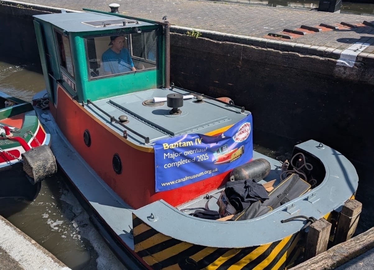 The Bantam IV tug in a lock on its way to Canal Cavalcade 2026. A sign attached to the front reads: Bantam IV Major overhaul completed 2025
