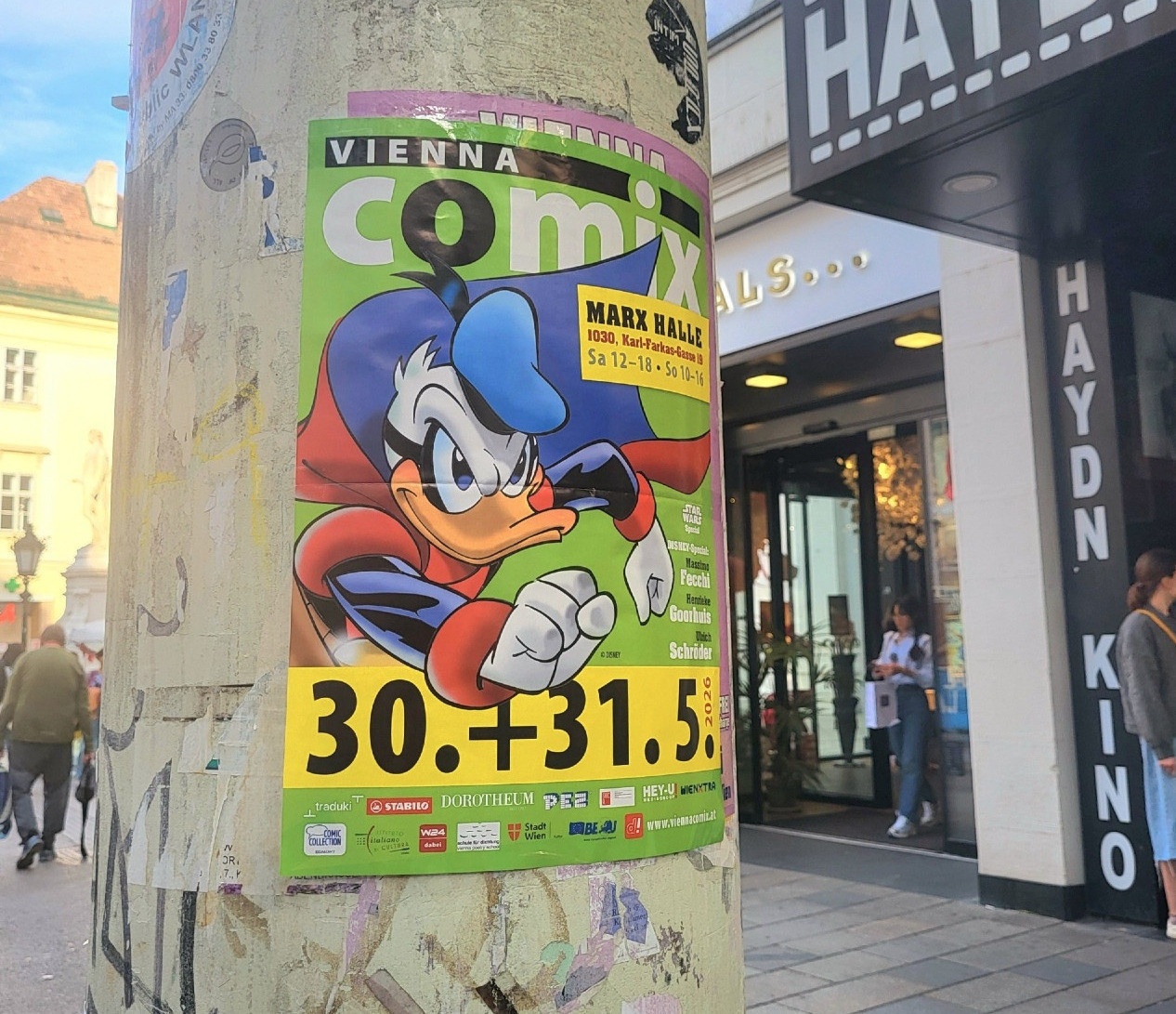 Vienna Comix poster pasted on a lamppost on the Mariahilferstrasse in Vienna in front of the Haydn English Cinema, with an image of Fantomiald (Duck Avenger).