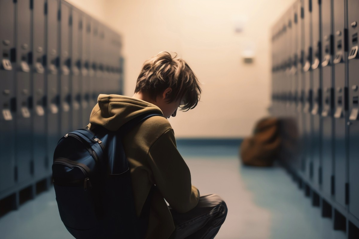 A young person sits with their back to the camera in a gloomy locker room