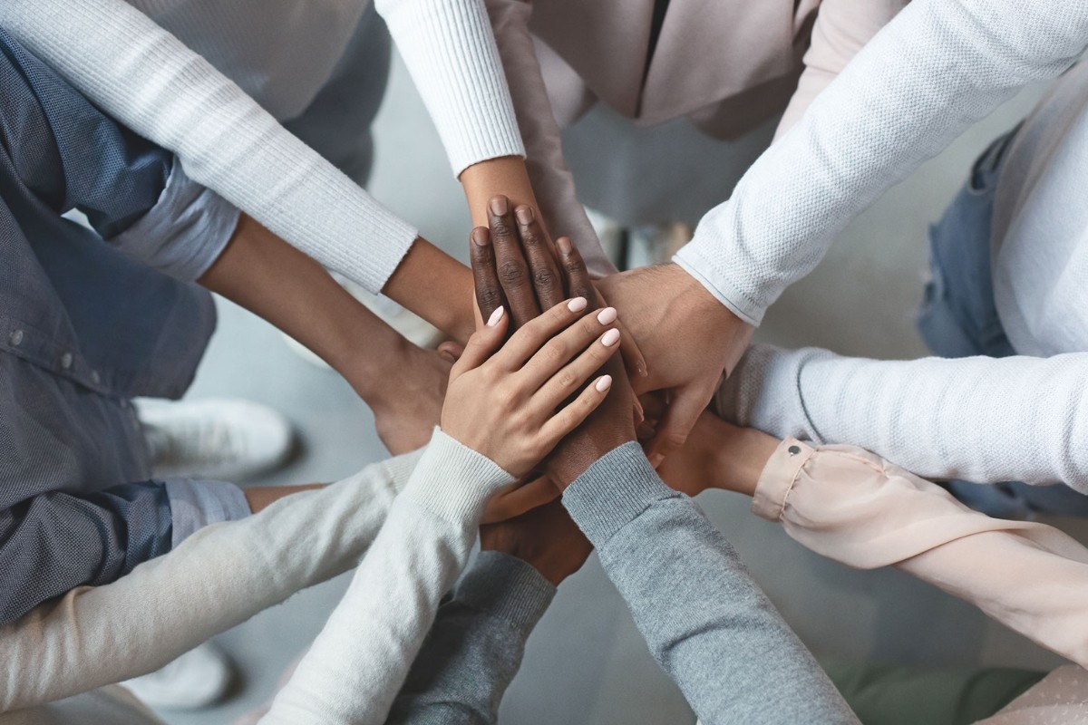 Close up of many hands of varying ethnicities ontop of each other in a circle.