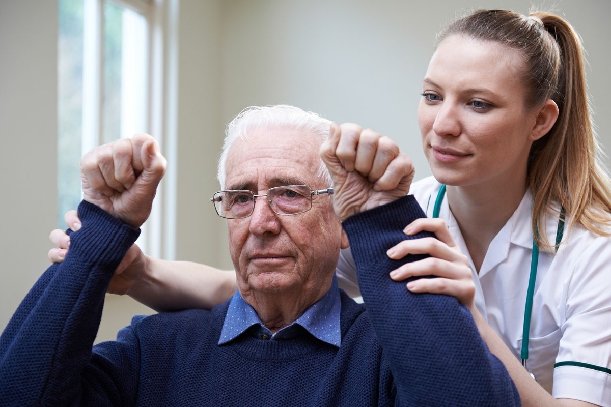 A Primary Care worker assists an elderly gentleman with some arm exercises