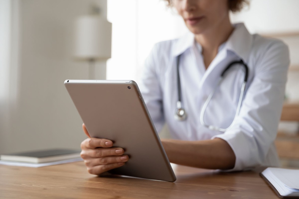 A GP sits at a desk looking at data on an electronic tablet