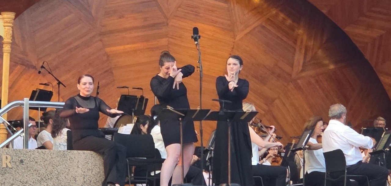 ASL interpreters Desiree Weems and Adri Neefus with Deaf youth performer Dotty on stage for Boston Landmarks Orchestra.