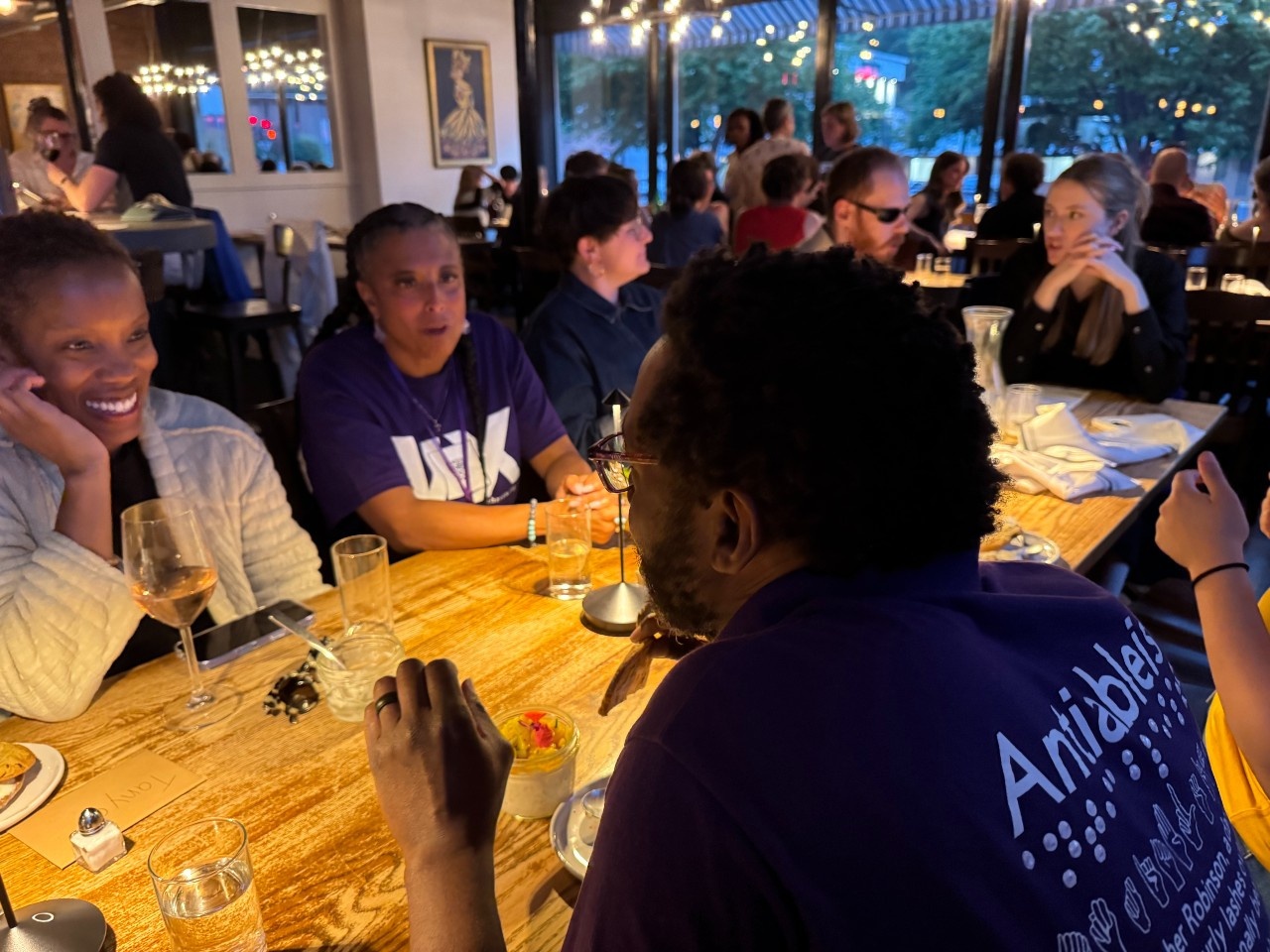 Group of Voxers and NAS folks sitting at a long dining table with scattered glasses and napkins in a dimly lit restaurant, including Christopher, Maria, and Tanya one of the facilitators.