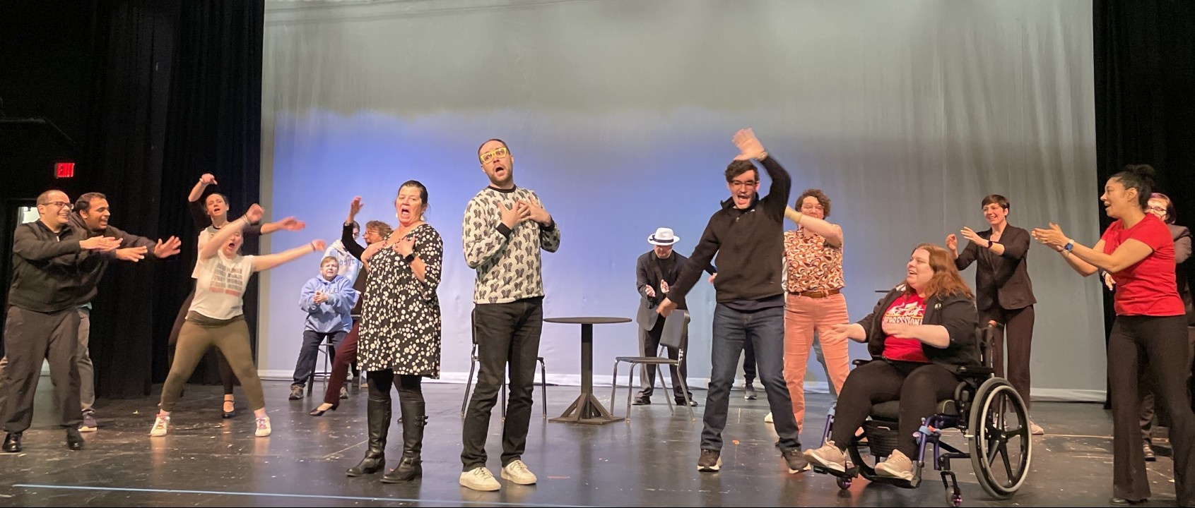 Wide shot of the cast of disabled, nondisabled, neurodivergent, neurotypical, LGBTQIA+ and ally actors of all ages rehearse on stage for The Prom