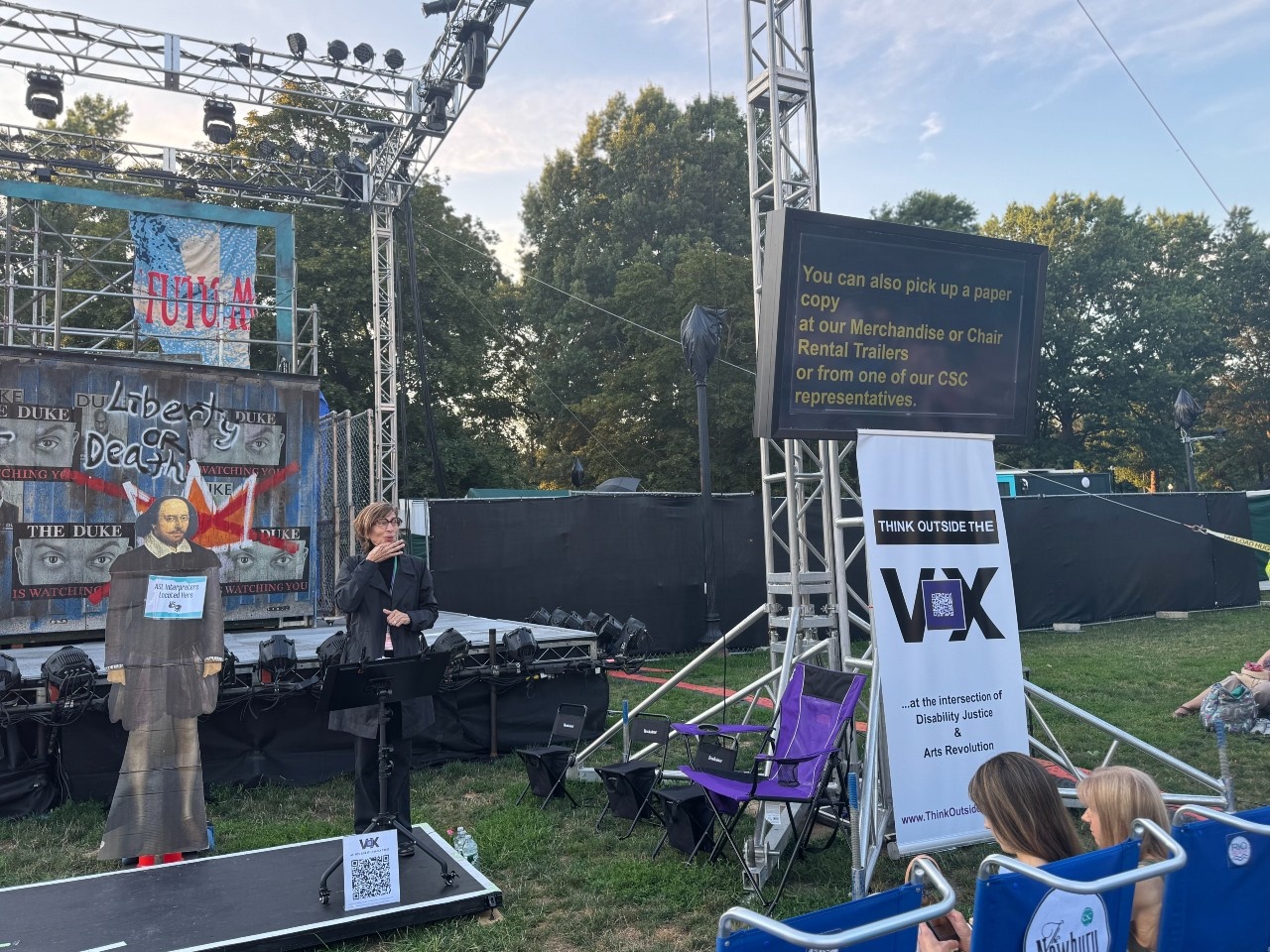 Kristin signing the ASL preshow for As You Like It with many access services and features surrounding her.