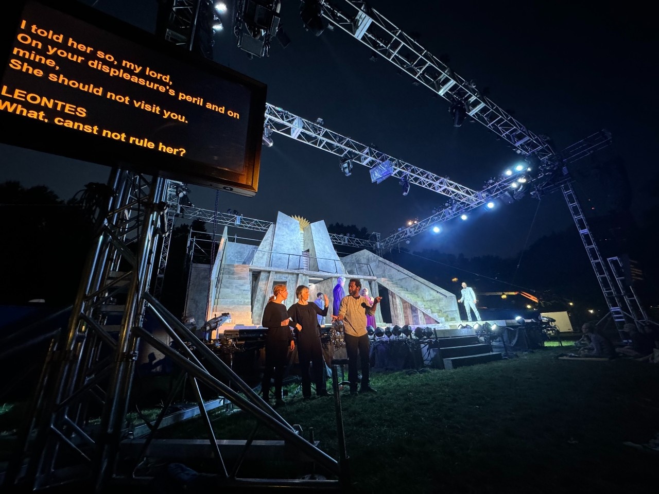 A wide lens shot of the DASL team in front of the stage right corner of the CSC stage at night. The stage features a side staircase, railings, and old castle-style, angular design, lined with light fixtures at the front. From left to right, the team: ASL