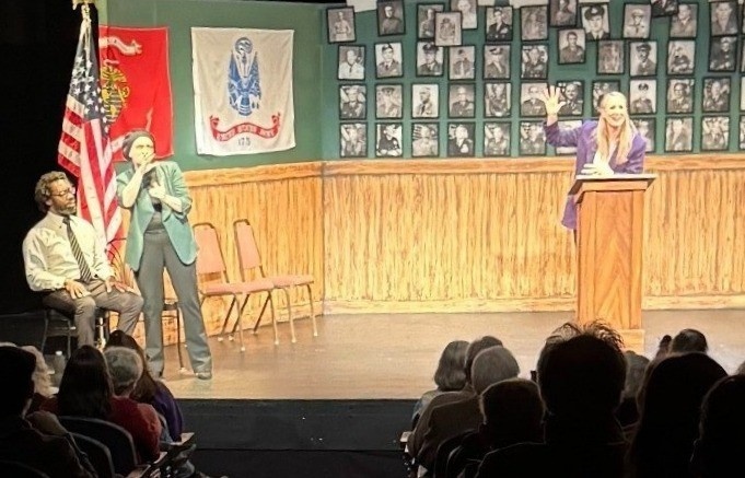 Desiree Weems interpreting on stage in ASL as the actor delivers her one woman show. Chris sits near Desiree, also on stage.