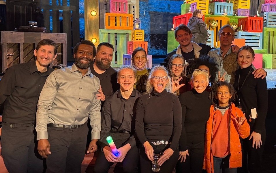 a large group photo of Deaf community, including Deaf DASLs, Deaf and hearing audience, ASL Interpreting team, family and friends standing together in front of the stage at Cutler Majestic Theater.