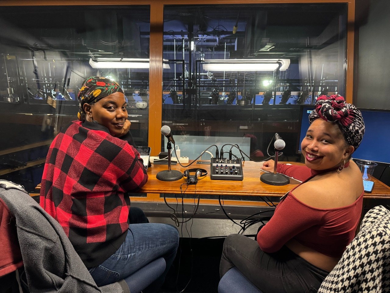 A photo of the AD team in the upper booth at The Calderwood. On the left, Mel Watkins, a Black woman who wears her hair wrapped in a floral scarf, dangly earrings...to access the full image description, click on the embedded