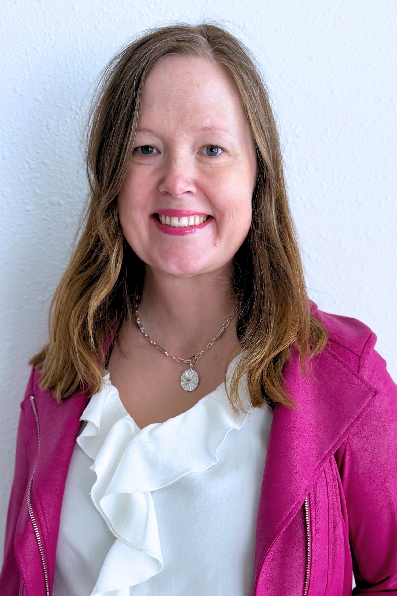 Photo of Cassie Ehrenberg, Executive Director of the Iron Horse Arts District. She wears a pink blazer over a white shirt and is smiling.