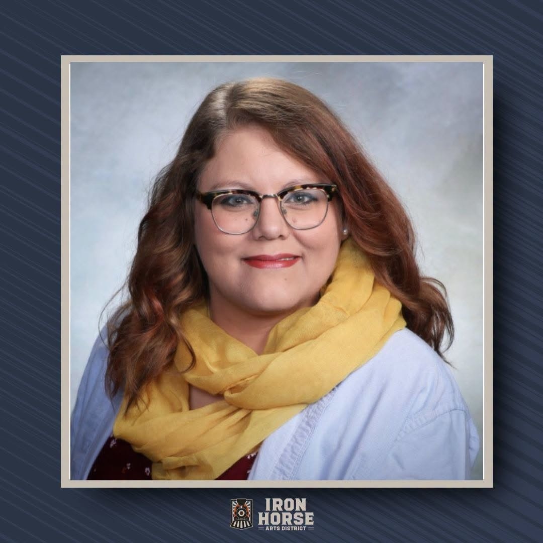Photo of Hannah Steen, newly hired Administrative Assistant for the Iron Horse Arts District. She is a brunette woman wearing a light blue shirt with yellow scarf and glasses.