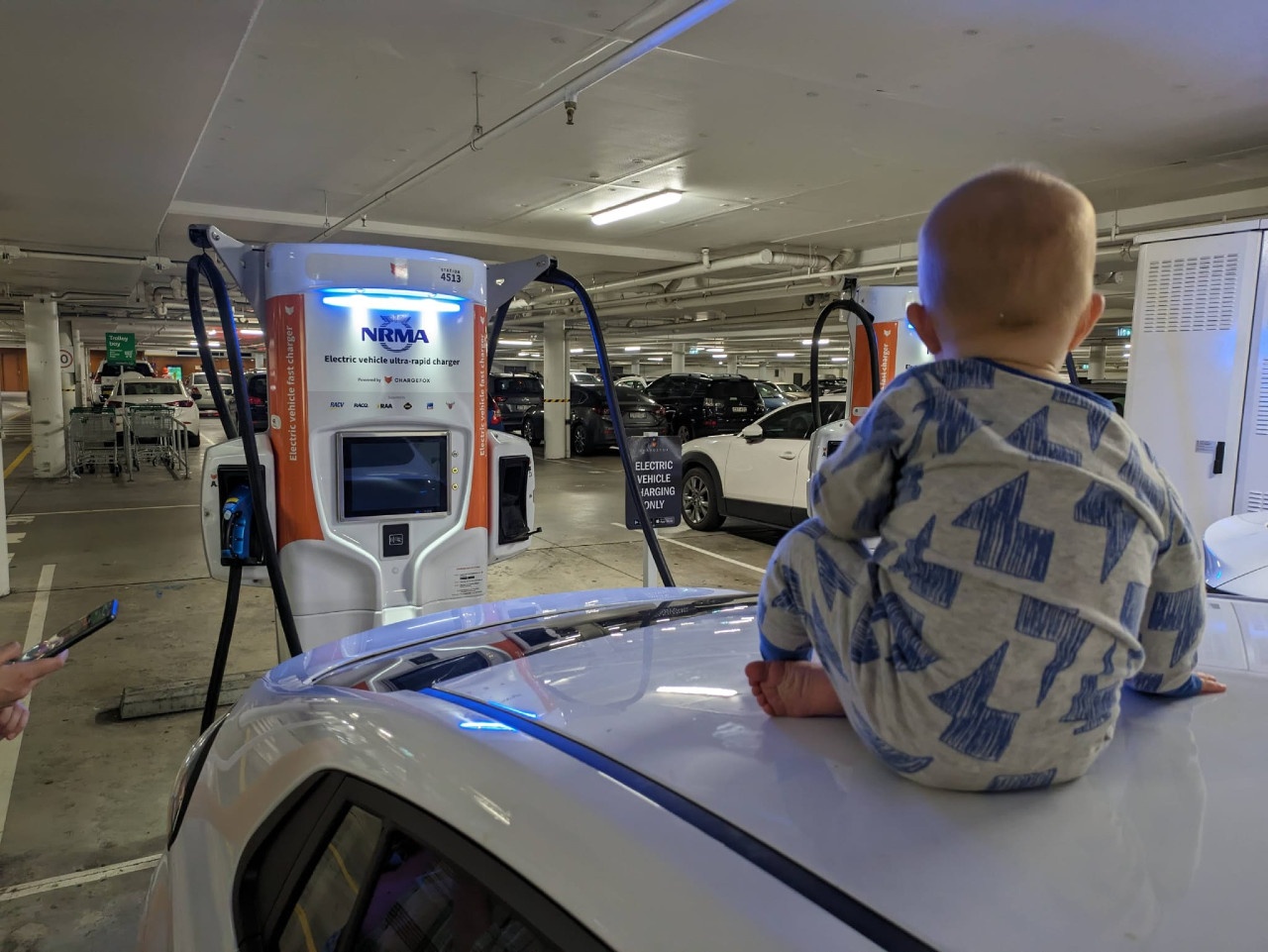 Matt and Alex's son sits on top of their Hyundai Electric during a fast-charging stop in Shell Cove.