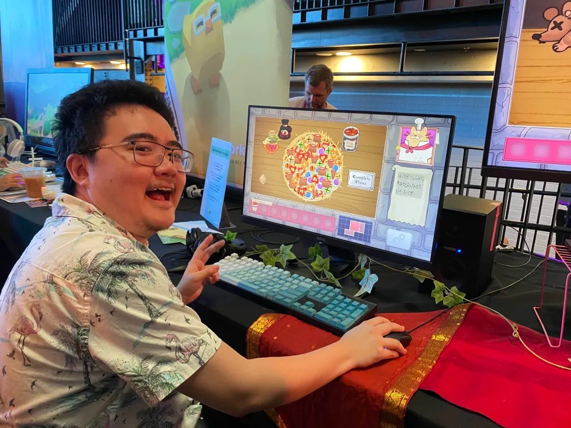 Image description: A happy gamer posing for a photo with his pizza on screen behind him.