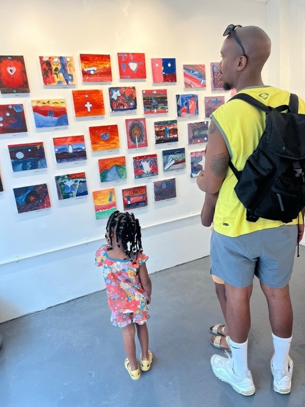 Visitors on opening day of the JOY exhibition. A father and daughter looking at a cluster of canvases on the wall.