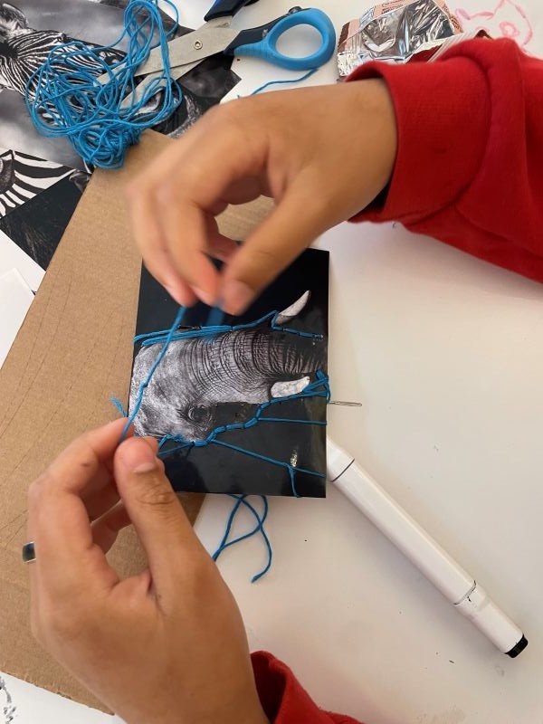 A close up of a young person's hands as they manipulate blue cotton thread as part of an embroidery
