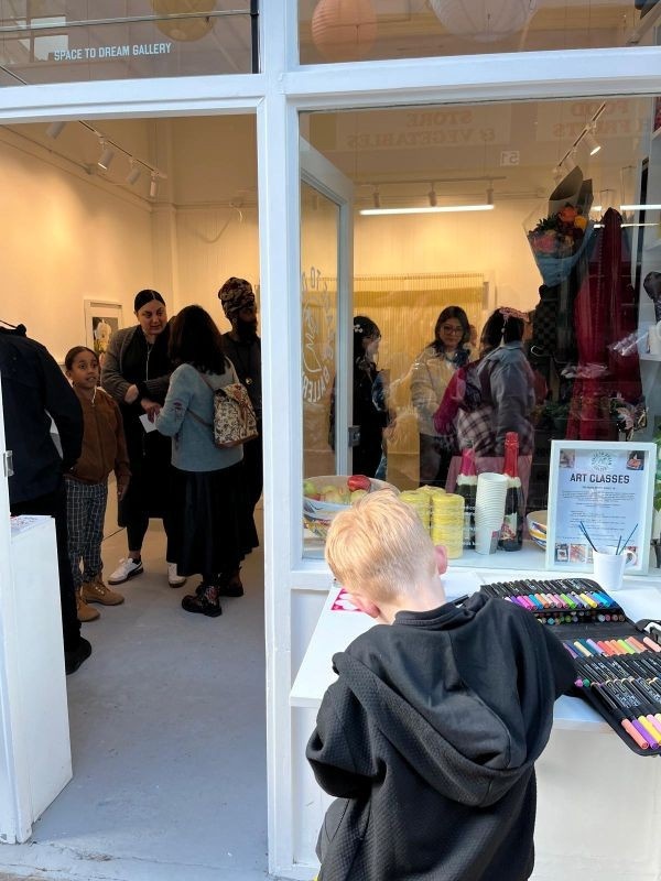 Photograph taken from just outside the Space to Dream gallery on the opening of the new exhibition; LIFE. In the foreground, a young boy is drawing, using the materials and table provided by the gallery while, in the background, the gallery is bustling wi