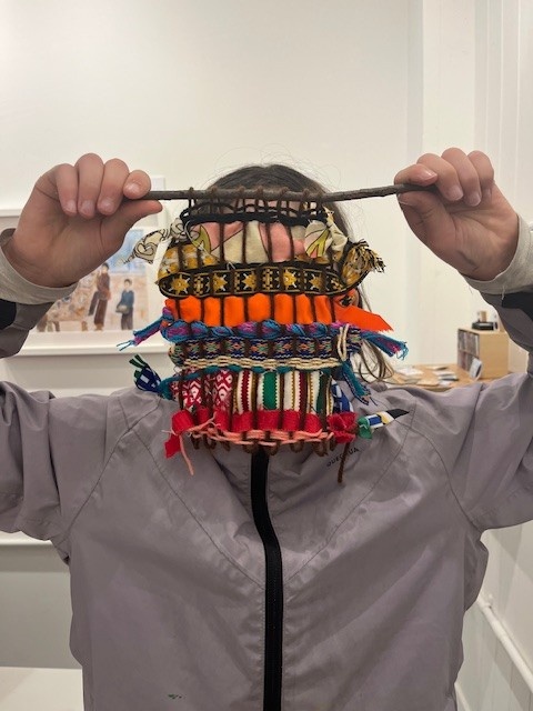 Photograph of a child showing off their weaving project in one of our art classes.