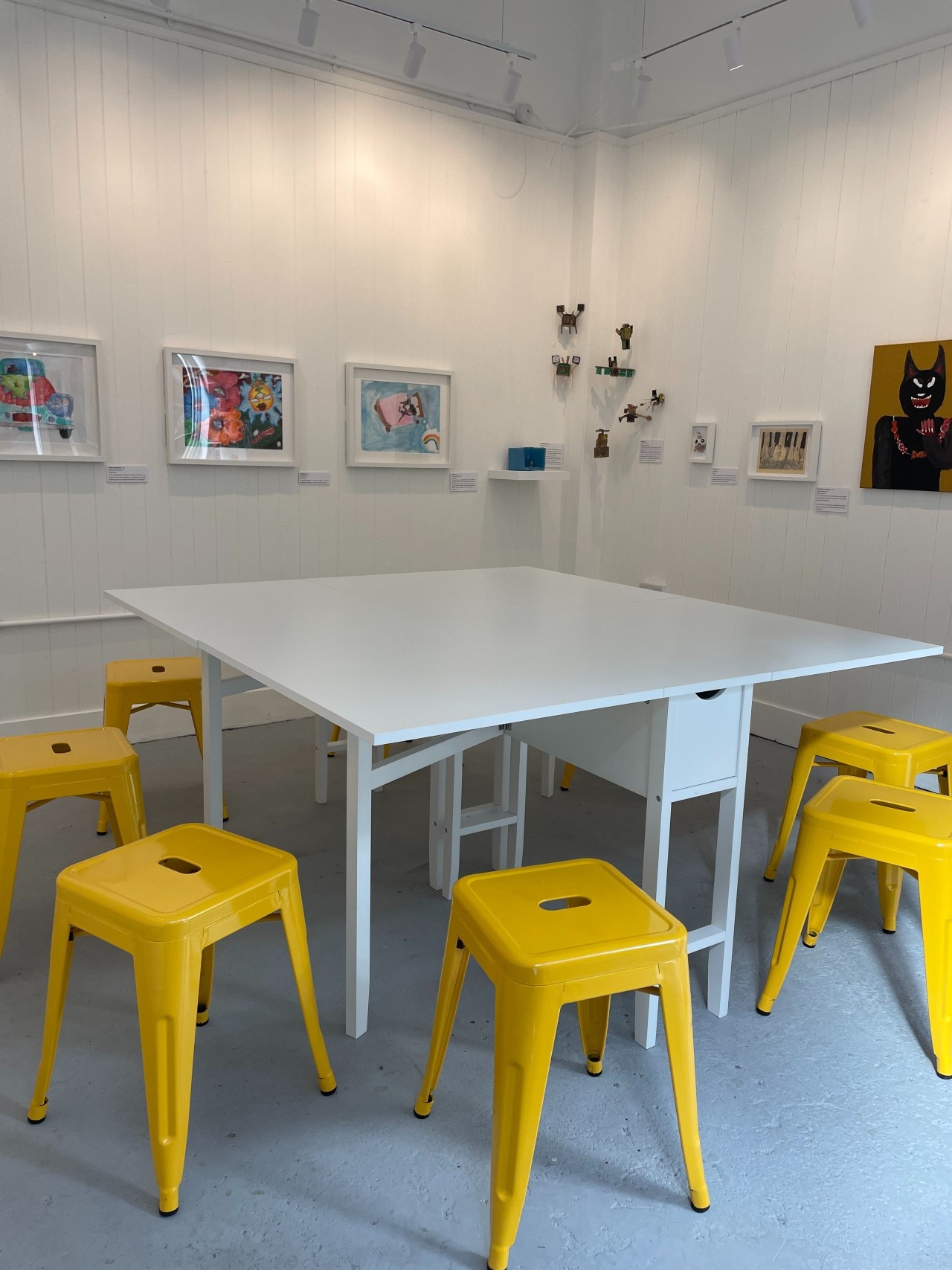 Photograph of our workshop table set up inside the gallery with our yellow stools. This will be where the art classes and workshops take place.