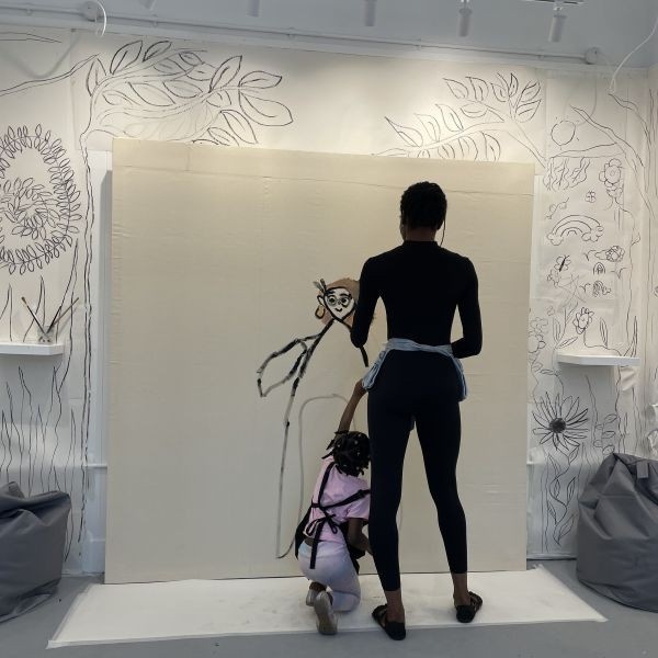 Morgane and Fran, both our co-founders, are standing in front of the Space to Dream gallery with arms outstretched. They are widely smiling. The photograph is stamped with Arts Council England's logo.