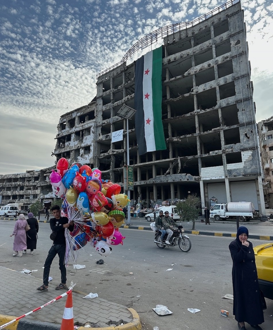Boy holding balloons with a backdrop of a bombed out building and the Syrian flag