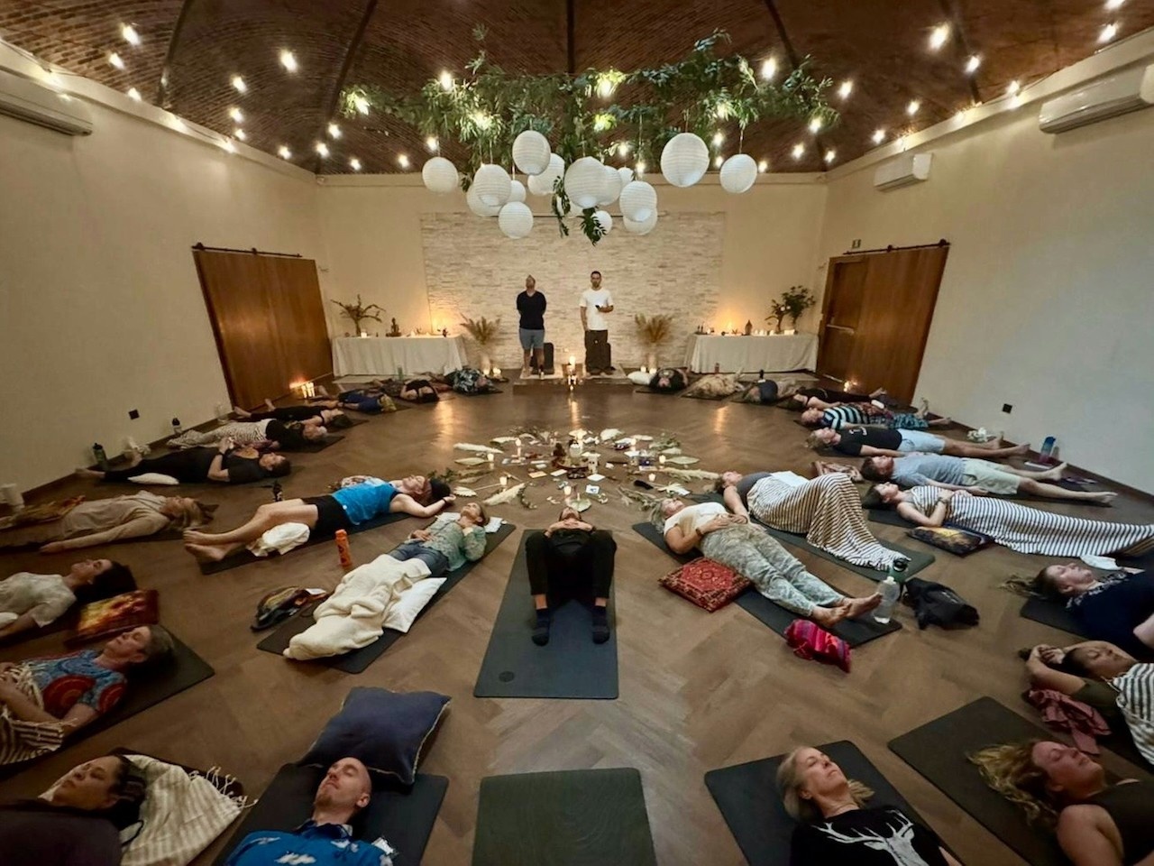 People lying down in a room filled with dimmed lights, candles, and mats