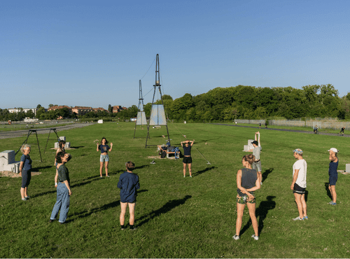 Eine Gruppe von Menschen stehen im Kreis auf dem Tempelhofer Feld bei der Hochseilanlage von den WireWalkers