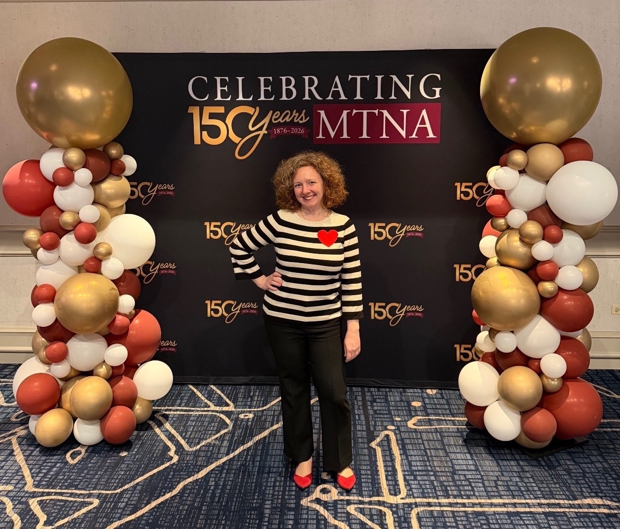Woman standing in front of MTNA banner with balloons on both sides.