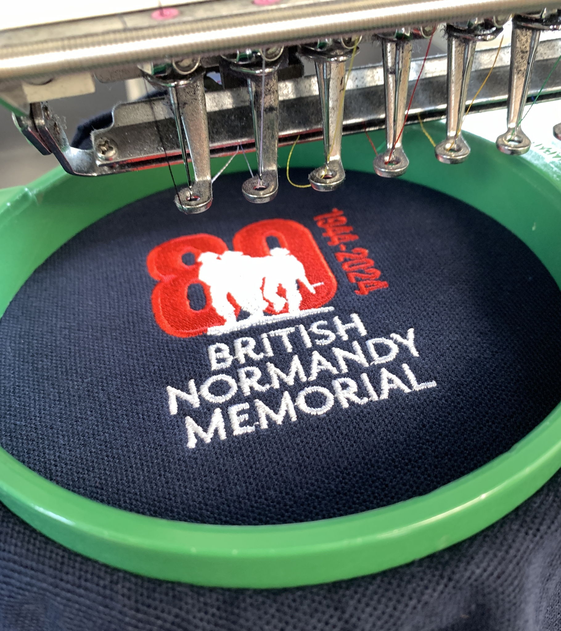 An embroidery machine stitching a British Normandy Memorial logo