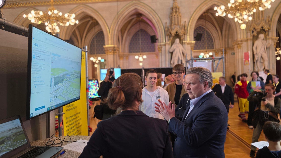 Bild: Bürgermeister Ludwig steht im Wiener Rathaus vor einem großen Bildschirm auf dem eine HORA 3D Hochwasservisualisierung zu sehen ist und unterhält sich mit VRVis-Forscherin Silvana Zechmeister