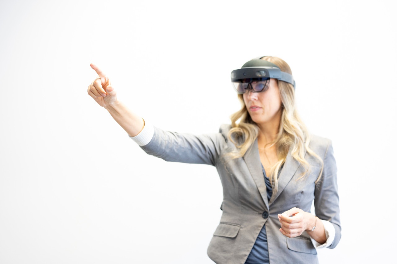 Bild: Forscherin Katharina Krösl trägt eine VR-Brille und zeigt mit der Hand auf einen Punkt im Raum