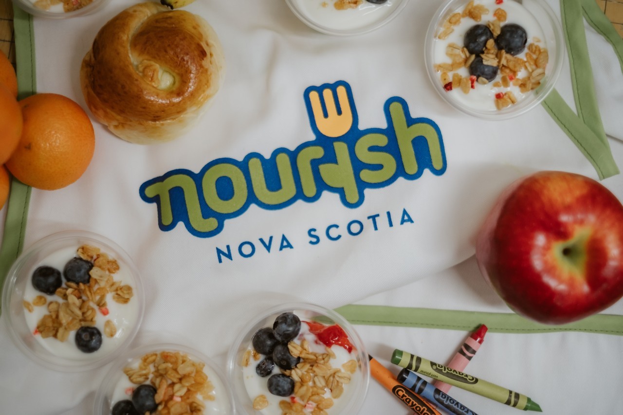 Nourish-branded apron sits behind an assortment of food items and crayons
