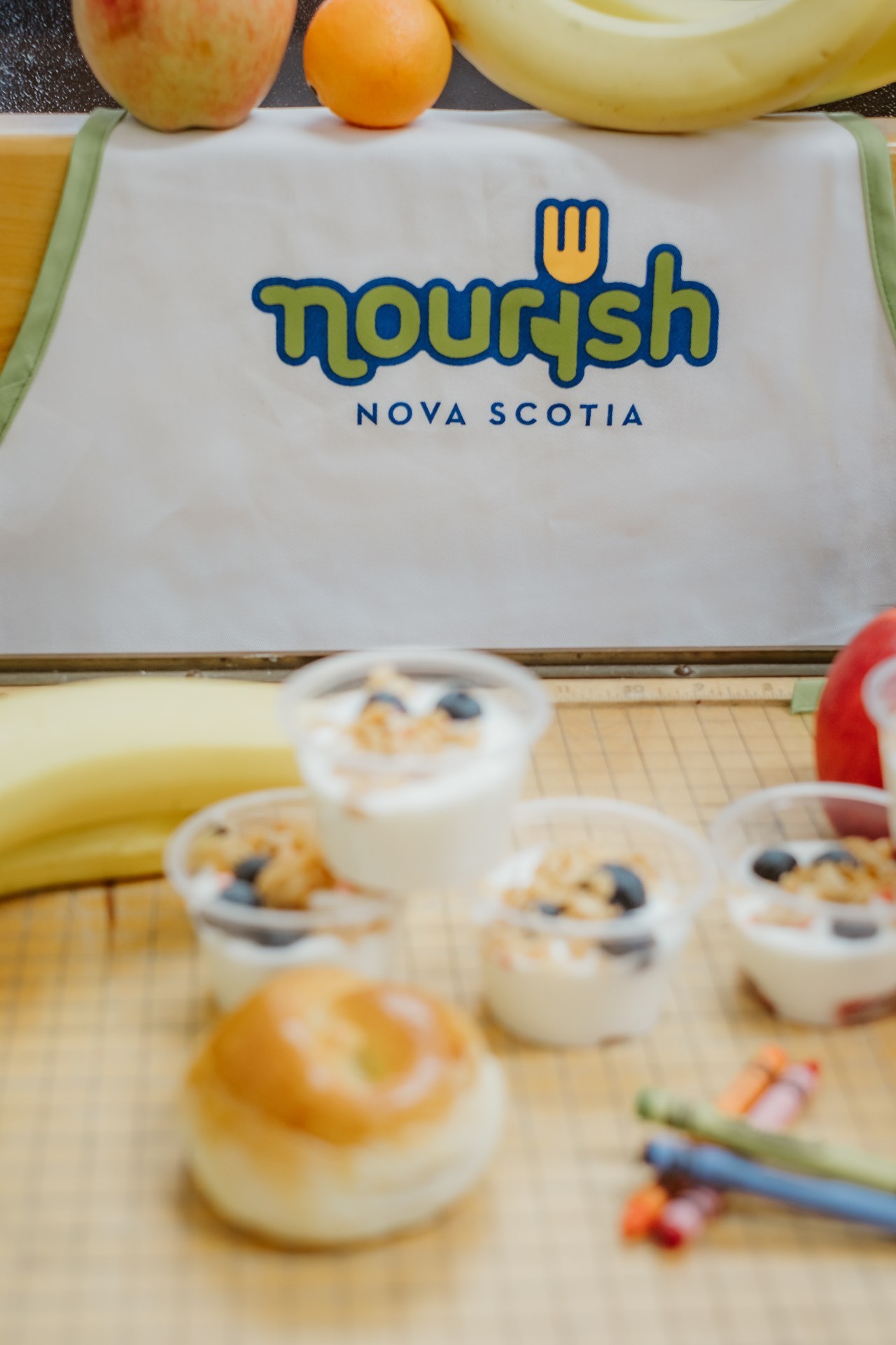 Nourish-branded apron sits behind an assortment of food items and crayons