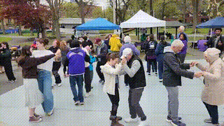 disabled and nondisabled patrons dance in pairs to merengue with alternating steps on the dance floor. others conversate in ASL, tactile, and spoken English. some dance solo or with a walker.